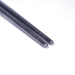 Two metal chopsticks with grooved grips are placed parallel to each other on a white surface.