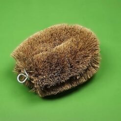 coconut tawashi cleaning brush with dense natural coir bristles and metal hanging loop on a green background