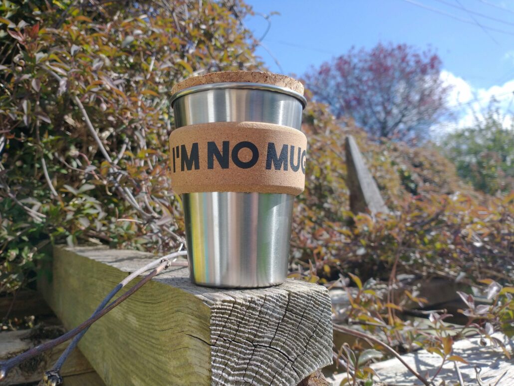 Plastic free stainless steel coffee cup with cork sleeve outdoors on a wooden fence