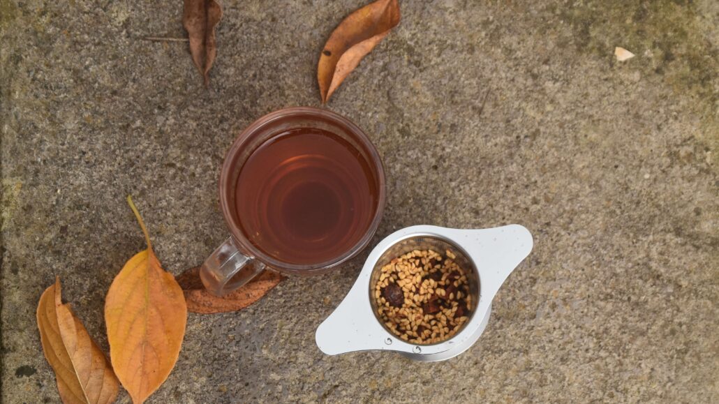 image of a cup of rosehip tea, with the ground rosehips in a cup infuser next to it