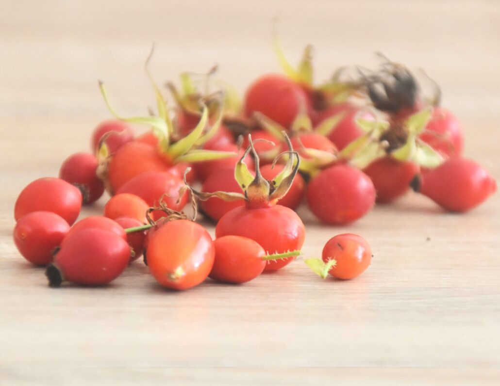 Image of a handful of rosehips strewn over a pale wooden tabletop