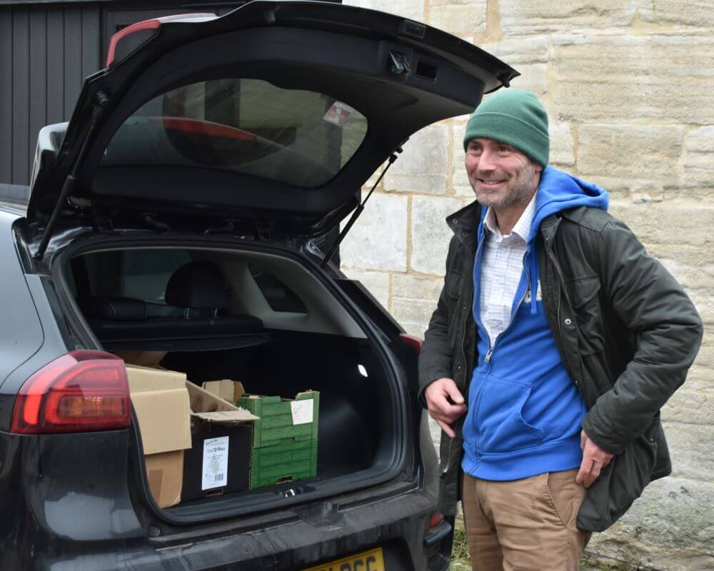 Image of a man standing next to his car, showing an open boot with card board boxes