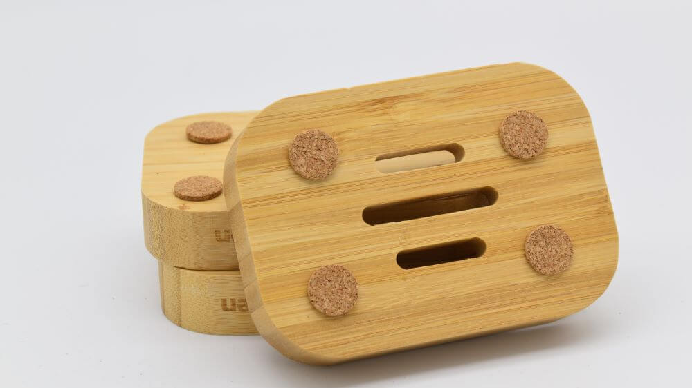 image of a bamboo soap dish, leaning against two other bamboo soap dishes, showing the botton, with cork bits