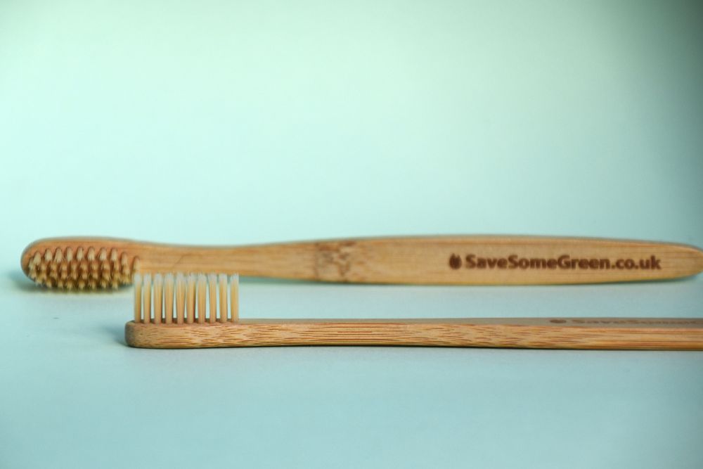 Image of two bamboo toothbrushes, one laying flat on it's back, one blurred in the background on its side, vaguely showing the words Save Some Green