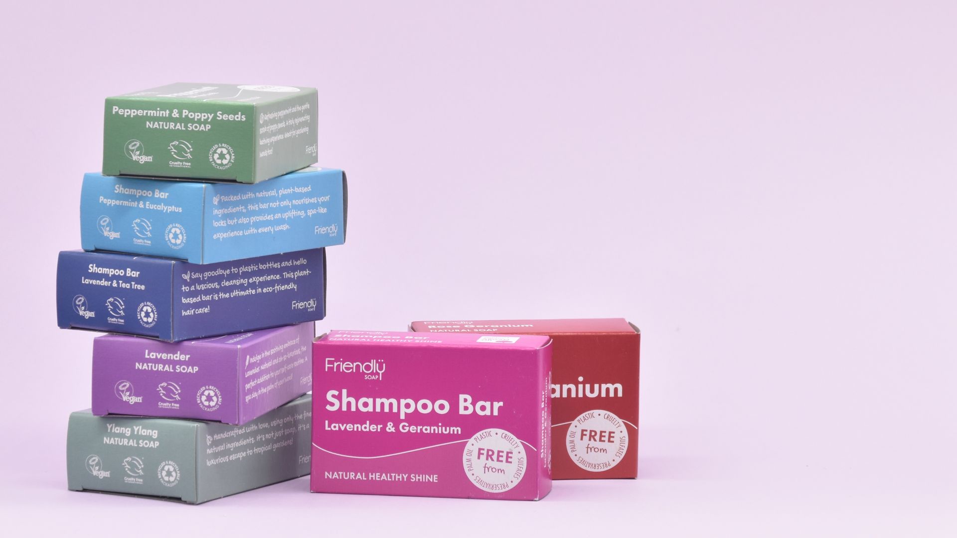 One pile of five different Friendly Soap and Shampoo Bars, with two bars standing to the left, all in boxes, against a lilac background.
