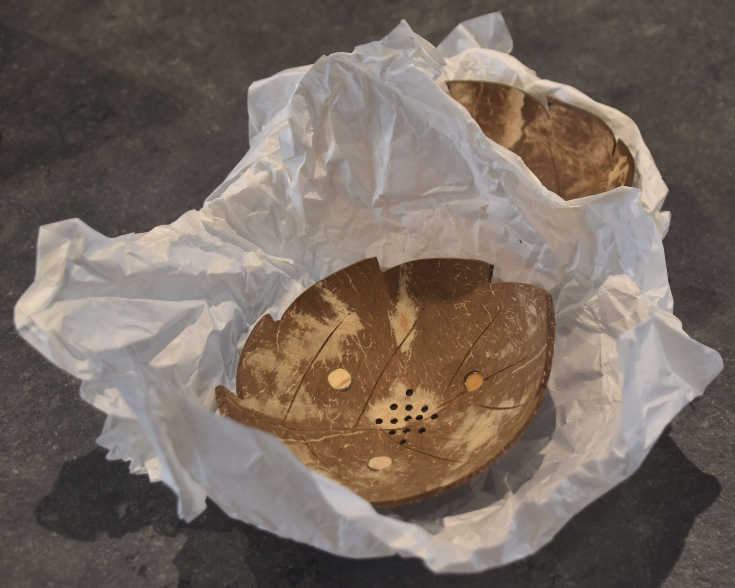 Image of a coconut soap dish, still in white wrapping paper, a second soap dish partially showing right behind it.