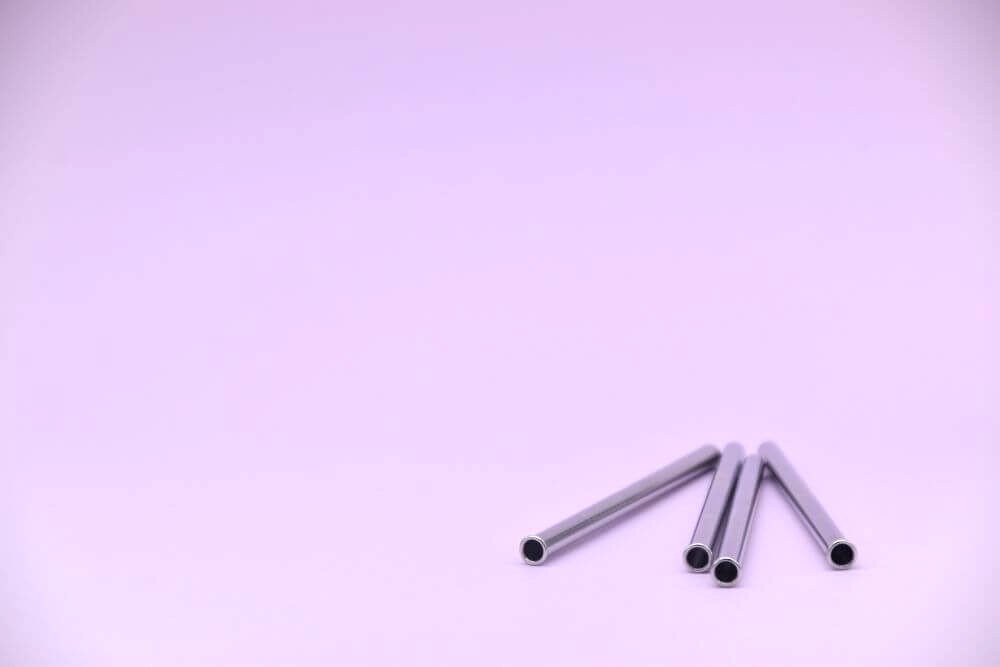Image of four stainless steel gin or cocktail straws, against a lilac background.