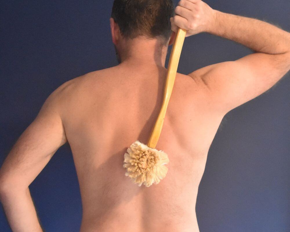 Image of a man dry brushing his back with a sisal back brush with a wooden handle.