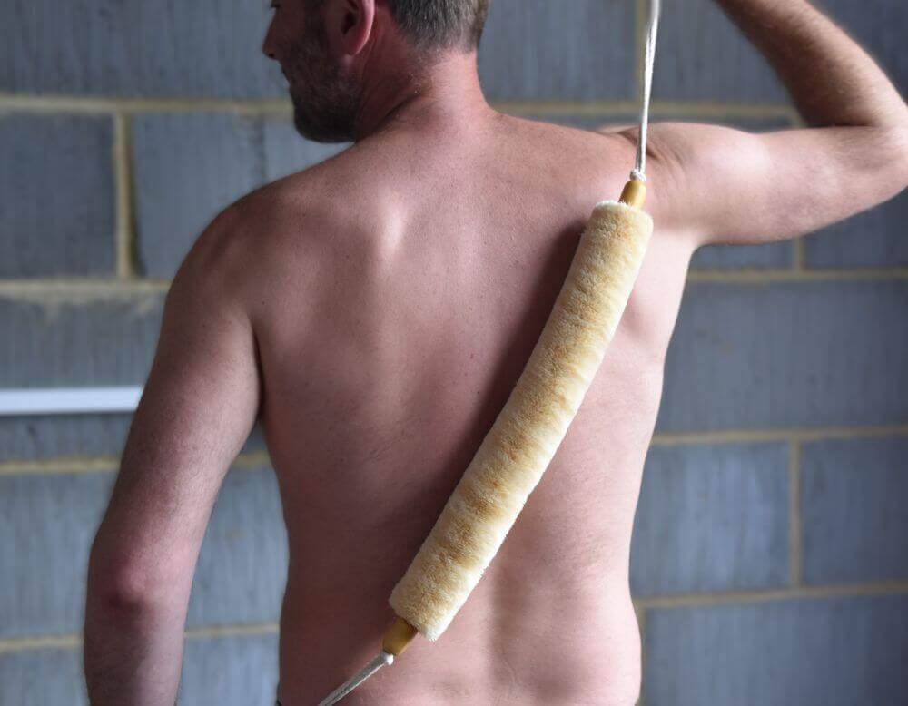 Image of a man dry brushing his back with a sisal back brush with ropes.