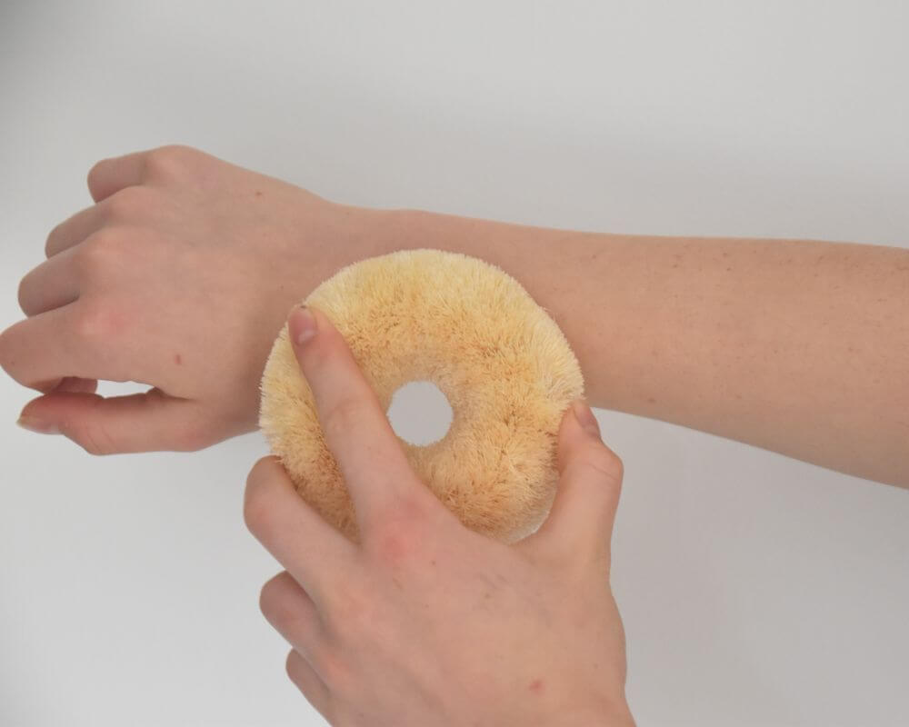 Image of a donut shaped sisal body brush being used for dry brushing an arm.