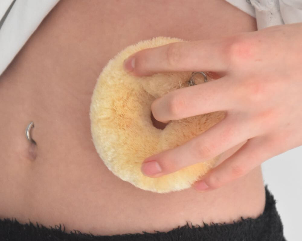 Image of a girl dry brushing her belly with a donut shaped sisal body brush.
