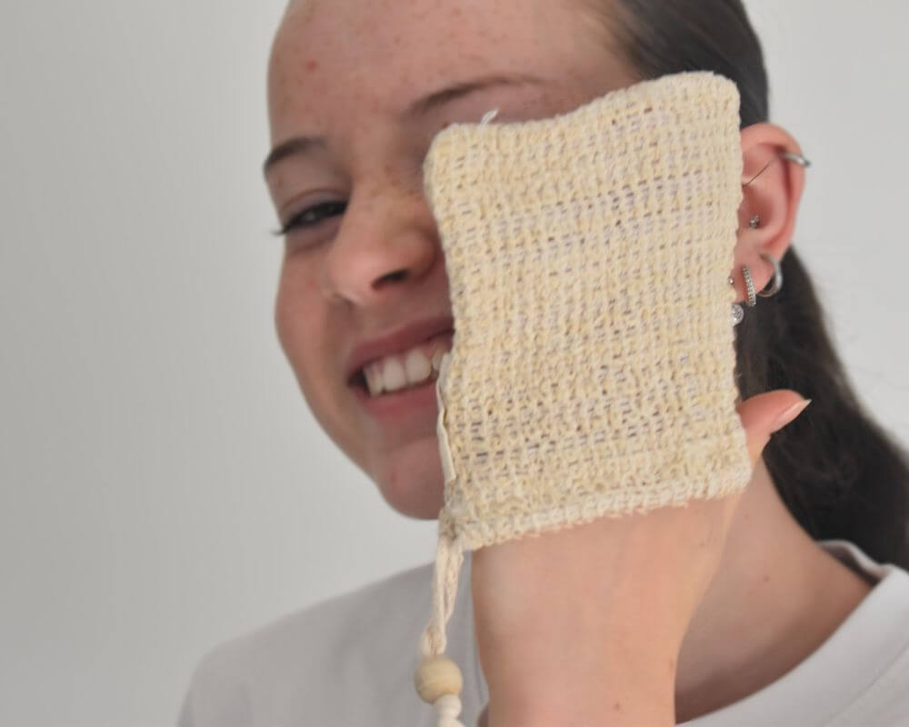 Image of a girl dry brushing her face with a sisal soap saver bag.